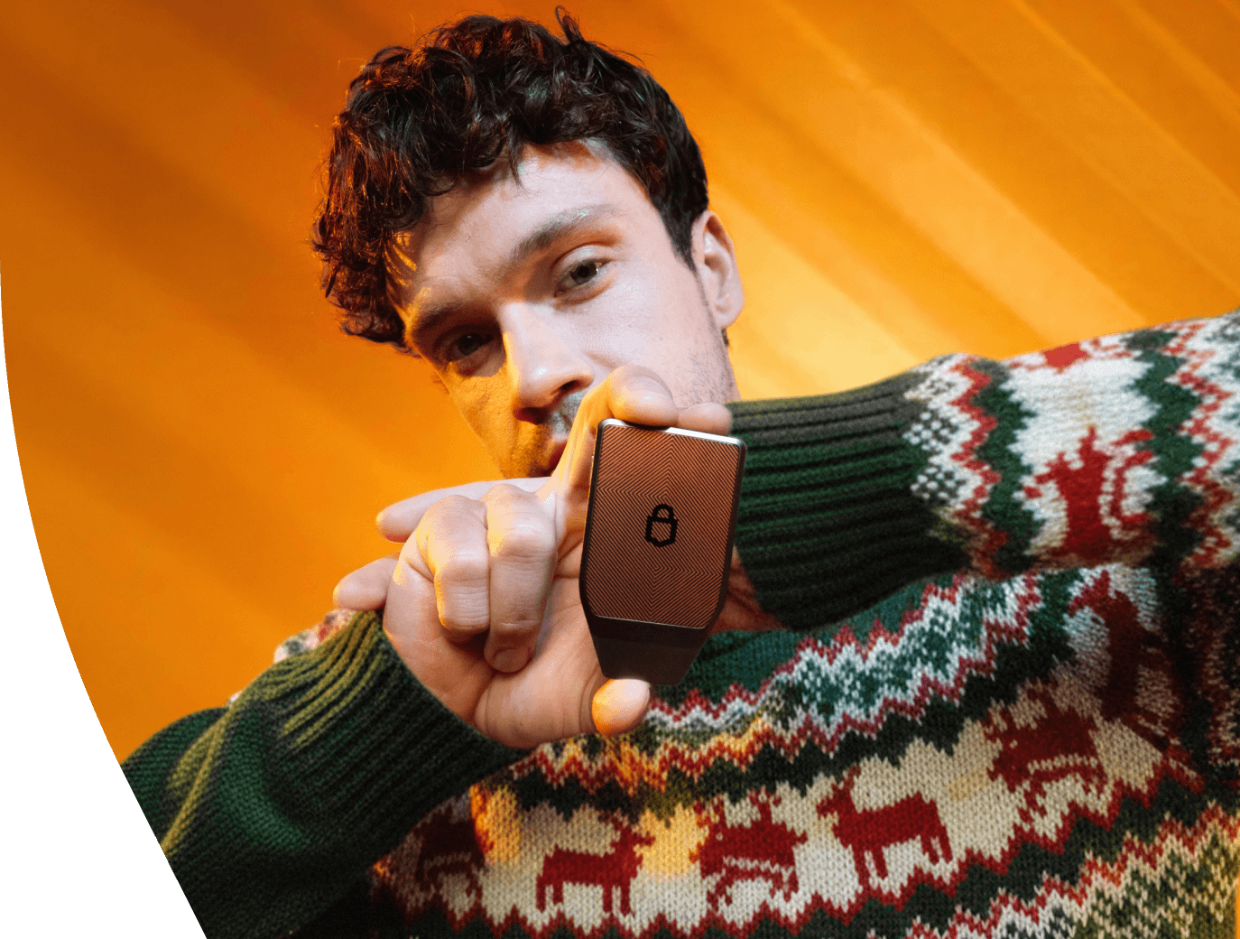 A man in a festive Christmas sweater holds up a Trezor Safe 7 hardware wallet, displaying the device against a warm orange background.